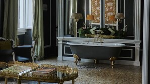 Une pièce aux couleurs noir et blanc, avec un canapé vert, une table à cadre doré et un grand miroir dont le reflet montre le canapé vert à l’arrière-plan.