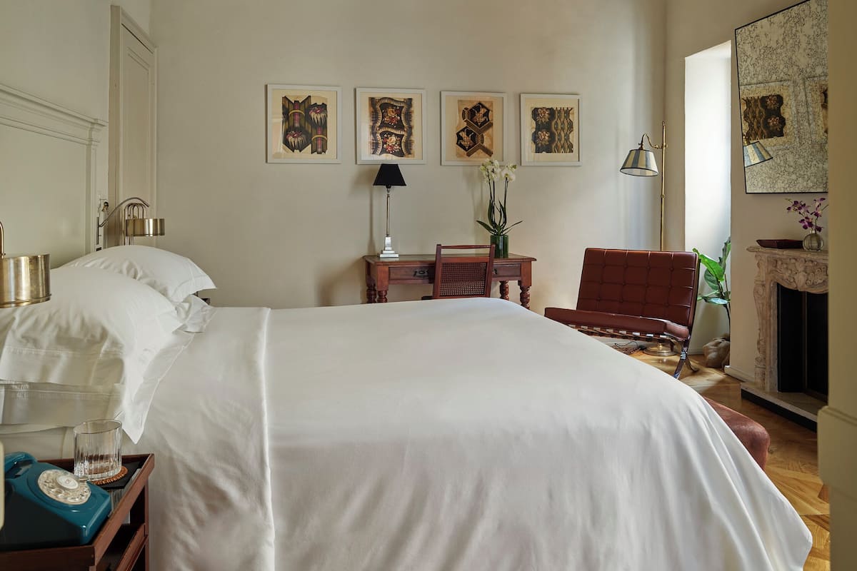 Un dormitorio con una cama grande, piso de madera, techo con azulejos decorativos, un escritorio con lámpara y cuadros en la pared.