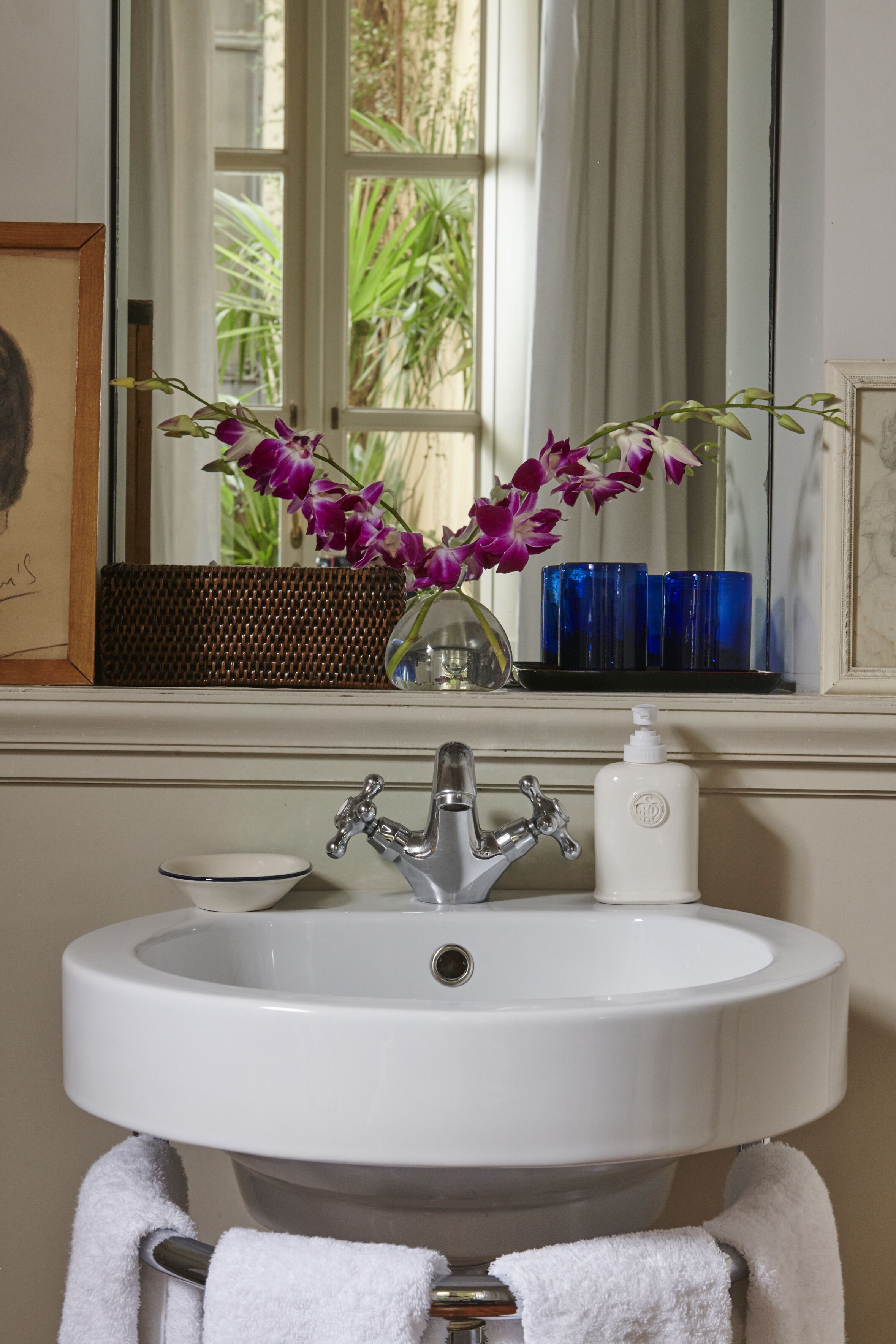 A bathroom with a white sink, a mirror, and a window with a view of greenery.