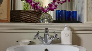 A bathroom with a white sink, a mirror, and a window with a view of greenery.