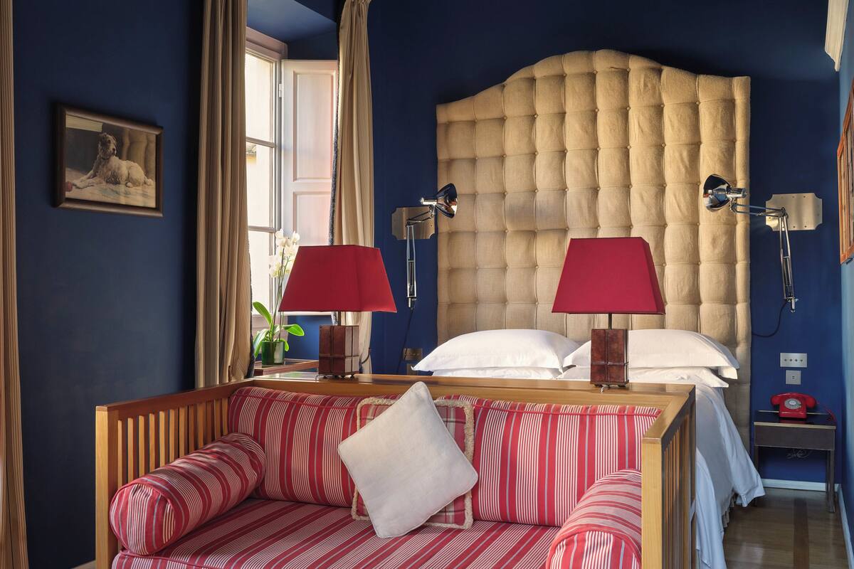 Habitación de hotel con una cama grande, un sofá, dos lámparas, una mesita de noche y un cuadro en la pared.