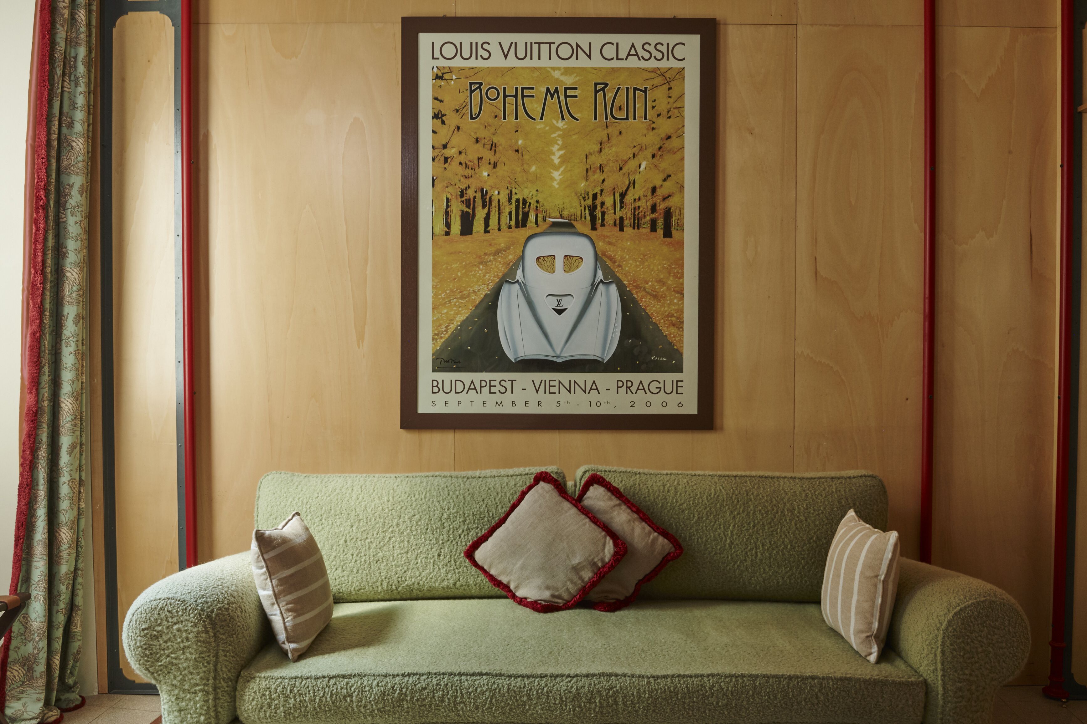 Ein gerahmtes Kunstwerk mit einem Zug an einer Wand über einem grünen Sofa mit zwei Kissen.