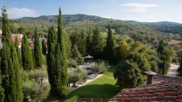 A courtyard with a gazebo, surrounded by tall cypress trees and a view of a hilly landscape.