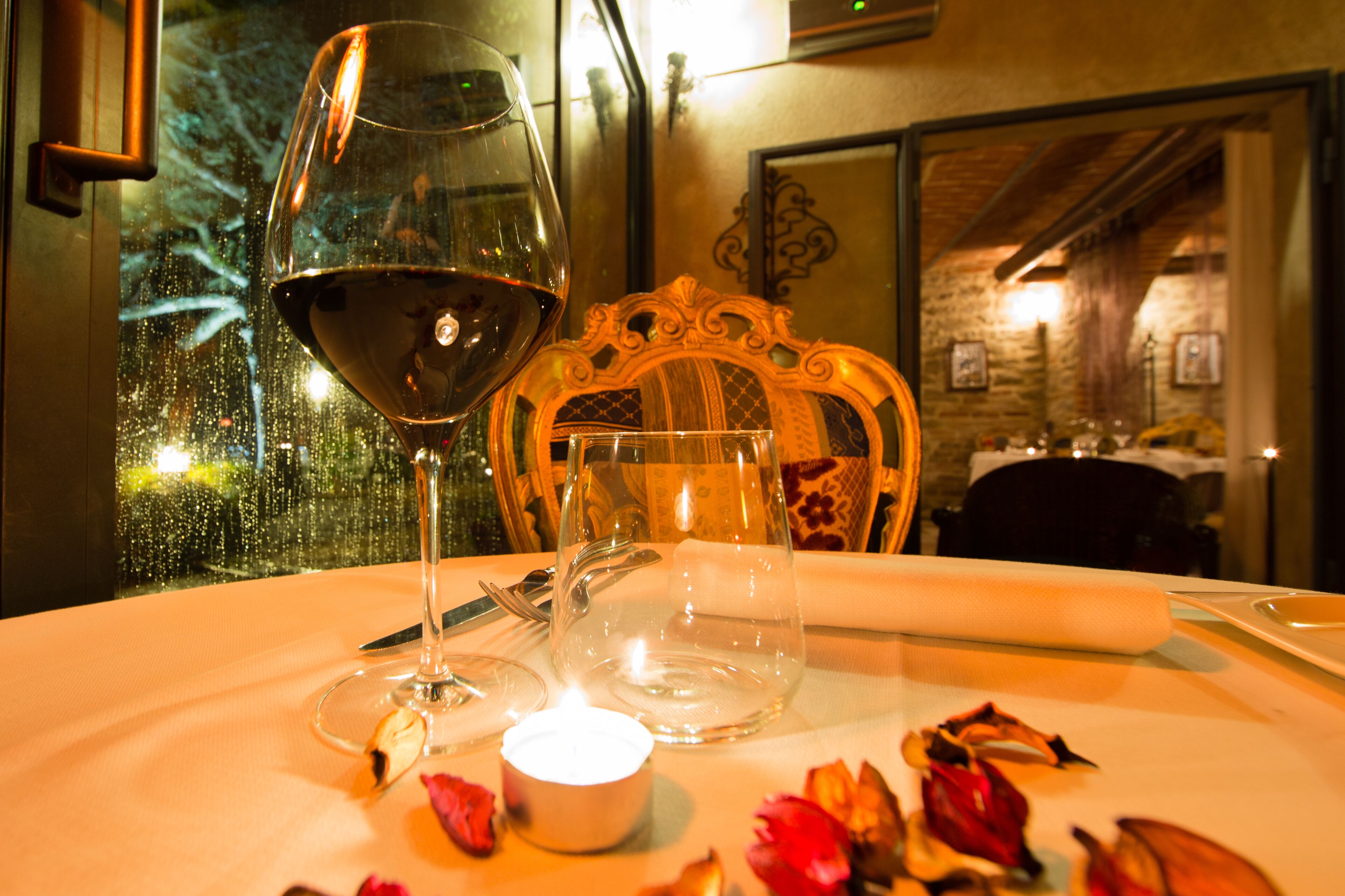 A dining table with a wine glass, candle, and rose petals.