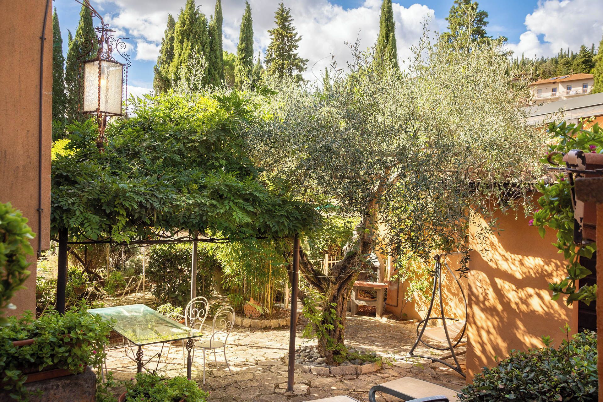 A courtyard with a table and chairs, surrounded by trees and a stone wall.