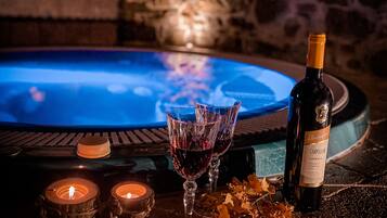 Un espace spa avec un mur en pierre, un jacuzzi, des bougies et une bouteille de vin posée sur une table.