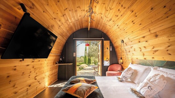 Una habitación acogedora tipo cabaña de madera con cama, almohadas, televisor y vistas al exterior.