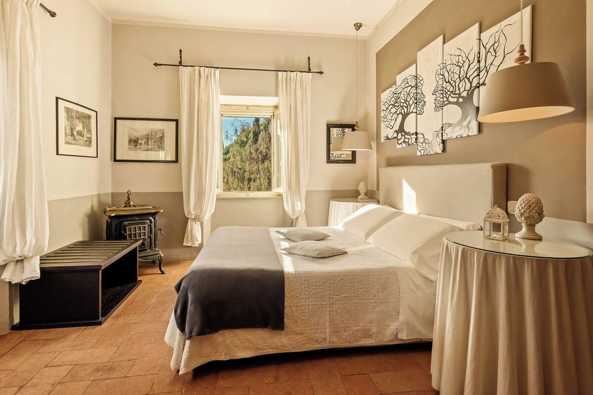 Un dormitorio con cama, mesita de noche, lámpara y una obra de arte en la pared.