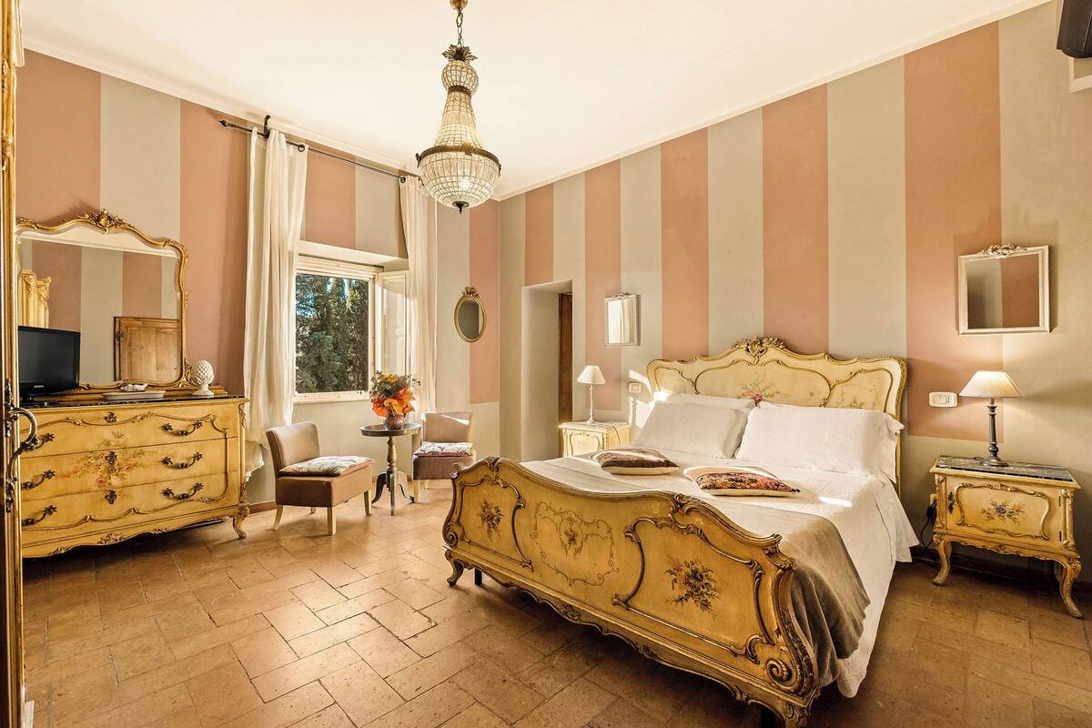 Una habitación con una cama grande y elaborada, un aparador, una silla y una mesa con un jarrón de flores.
