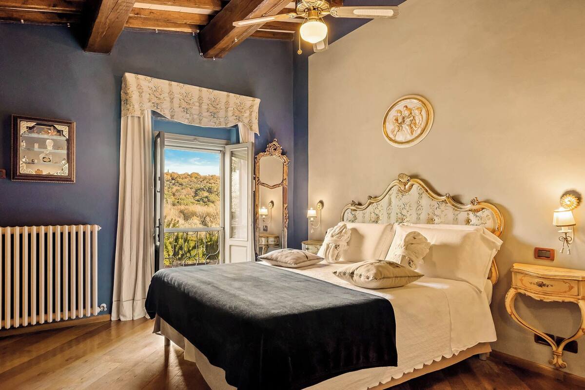 Un dormitorio con una cama grande, vistas al exterior por una ventana, un radiador y techo de madera.
