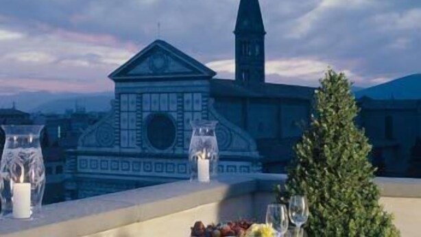 A dining table with candles and a view of a building with a clock tower. - Palazzo Vecchio (Florence)