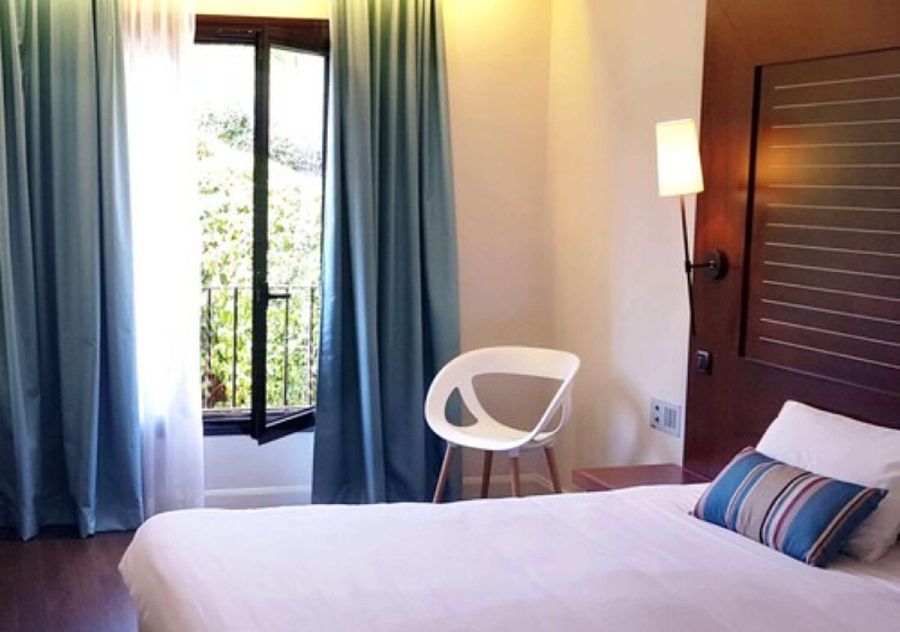 Ein Hotelzimmer mit Bett, Stuhl, einem Fenster mit Vorhängen und einer Tür.