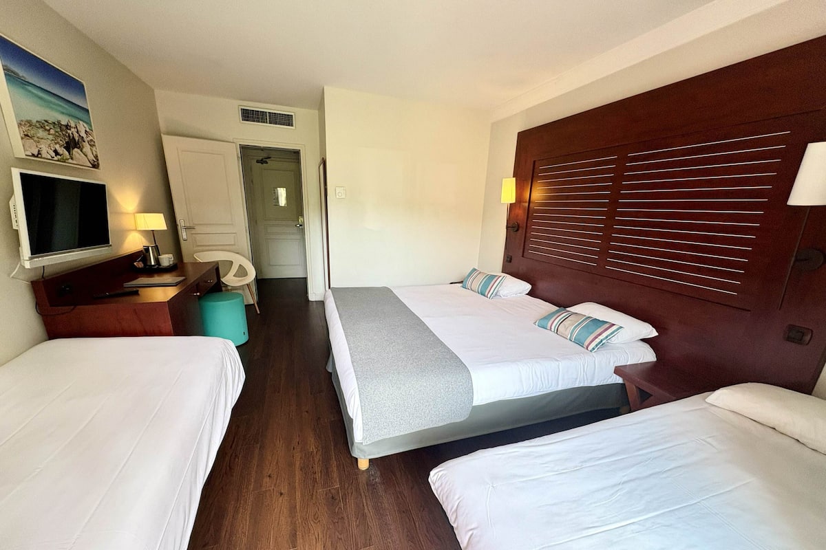 A hotel room with two beds, a TV, a desk with a lamp, and a door leading to a bathroom.