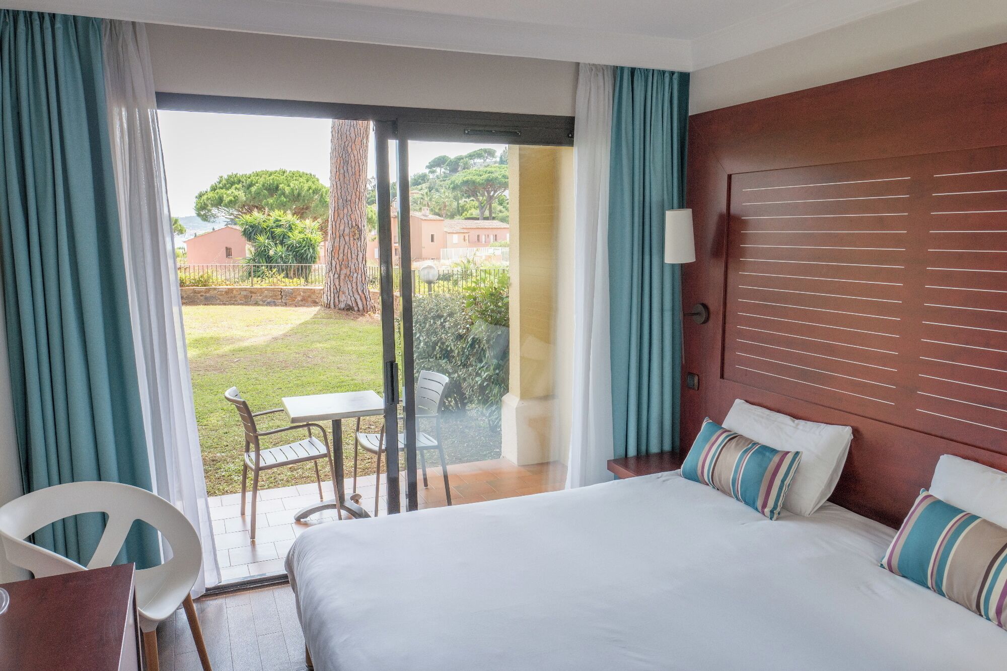A hotel room with a bed, a table, chairs, and a view of the outside.