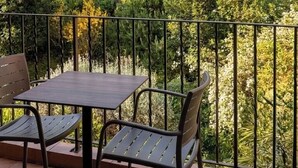 A balcony with a table and chairs, overlooking a landscaped garden with various trees and shrubs.