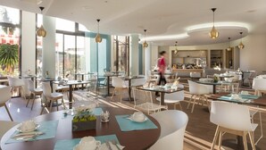 A modern restaurant with round tables, white chairs, and pendant lighting.
