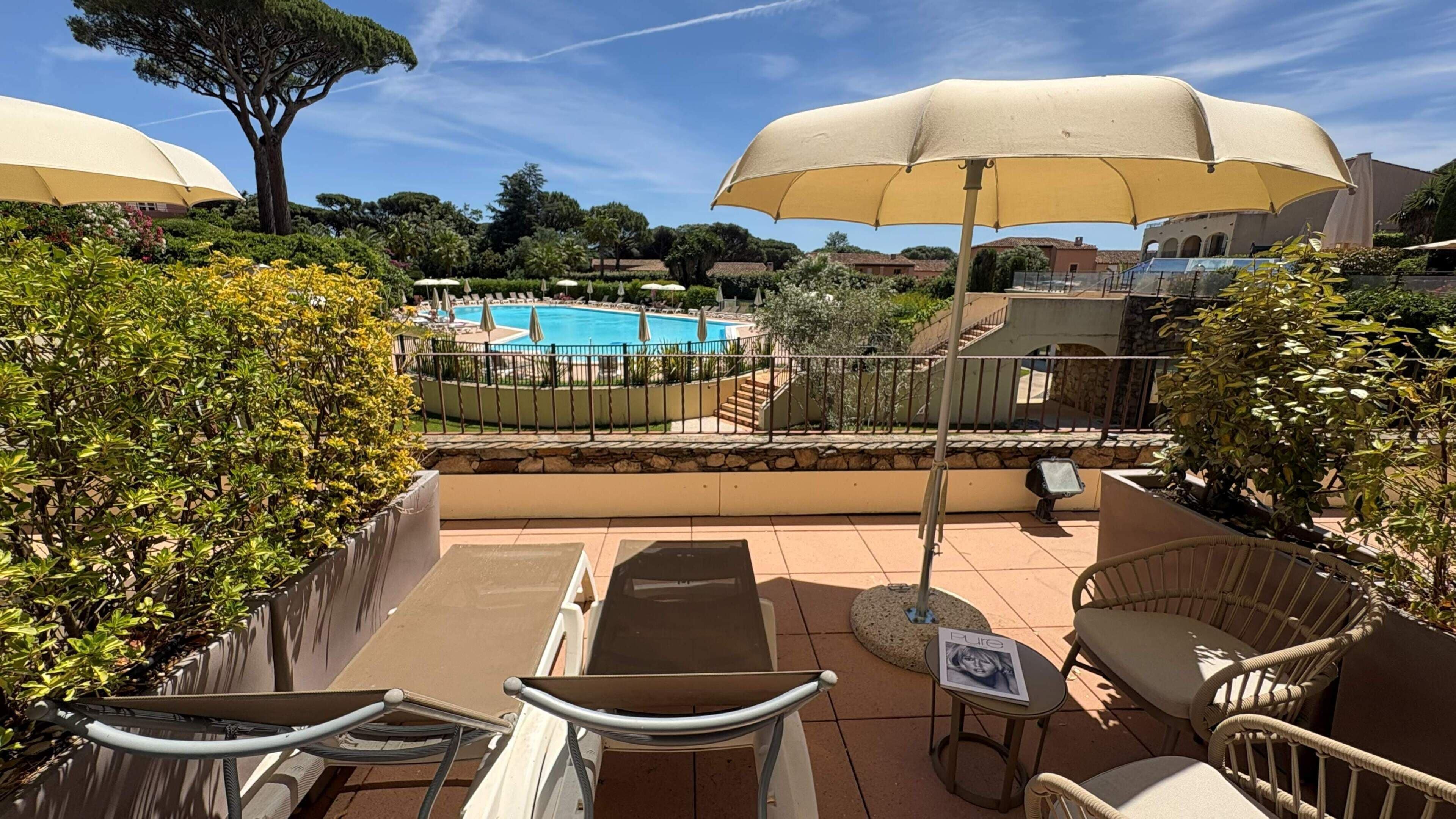 Zona junto a la piscina con sillas de descanso, sombrillas y vista a una alberca.