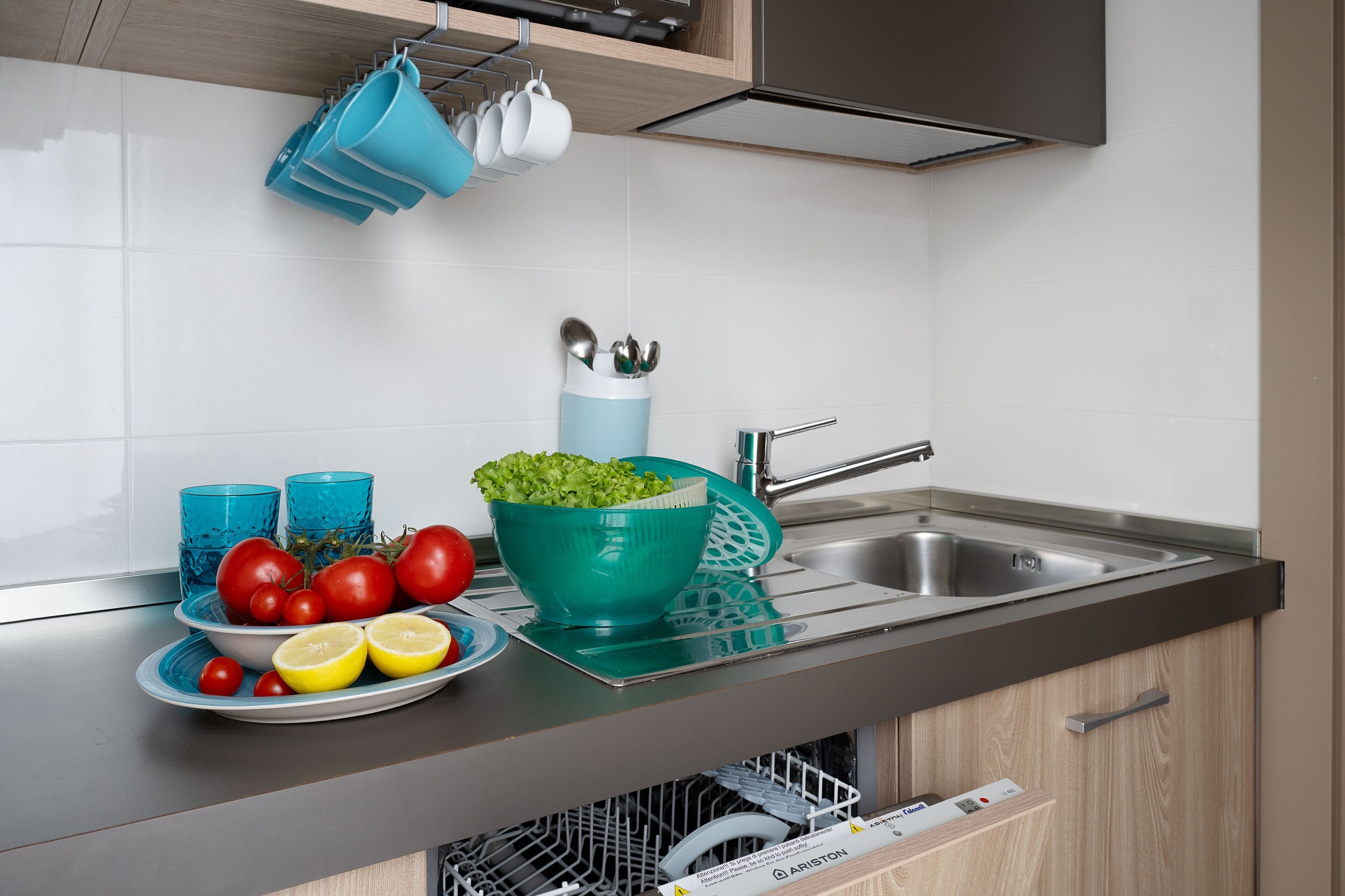A modern kitchen with a stainless steel sink, a dish rack, and a bowl of green salad.