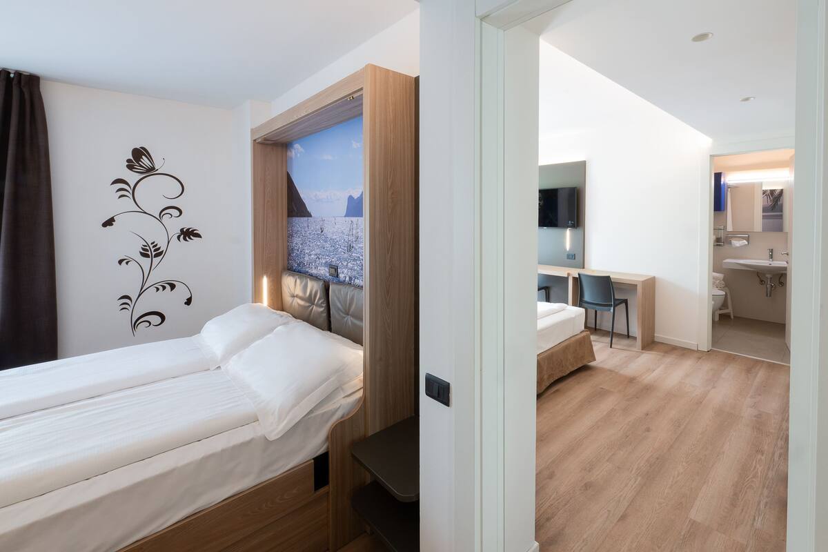 Une chambre moderne avec un lit simple, un bureau et une salle de bain visible à travers une porte ouverte.