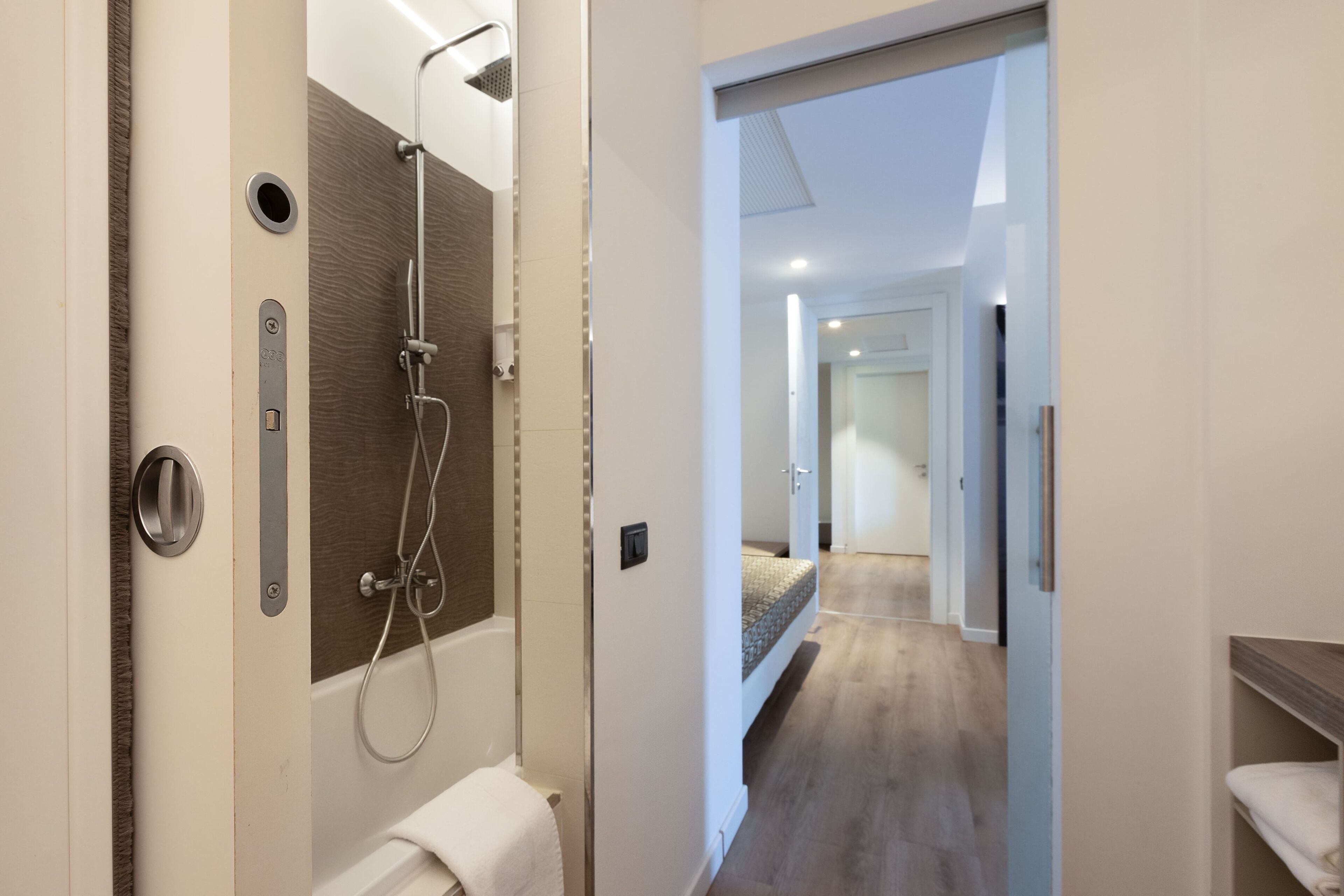 Un baño moderno con ducha, inodoro y lavabo. Hay un pasillo que conduce a otra habitación.
