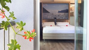 Een hotelkamer met een bed, een schilderij van een landschap en een plant met rode bloemen.