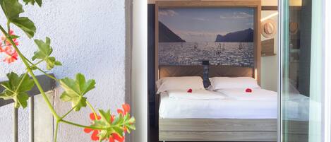 A hotel room with a bed, a painting of a landscape, and a plant with red flowers.