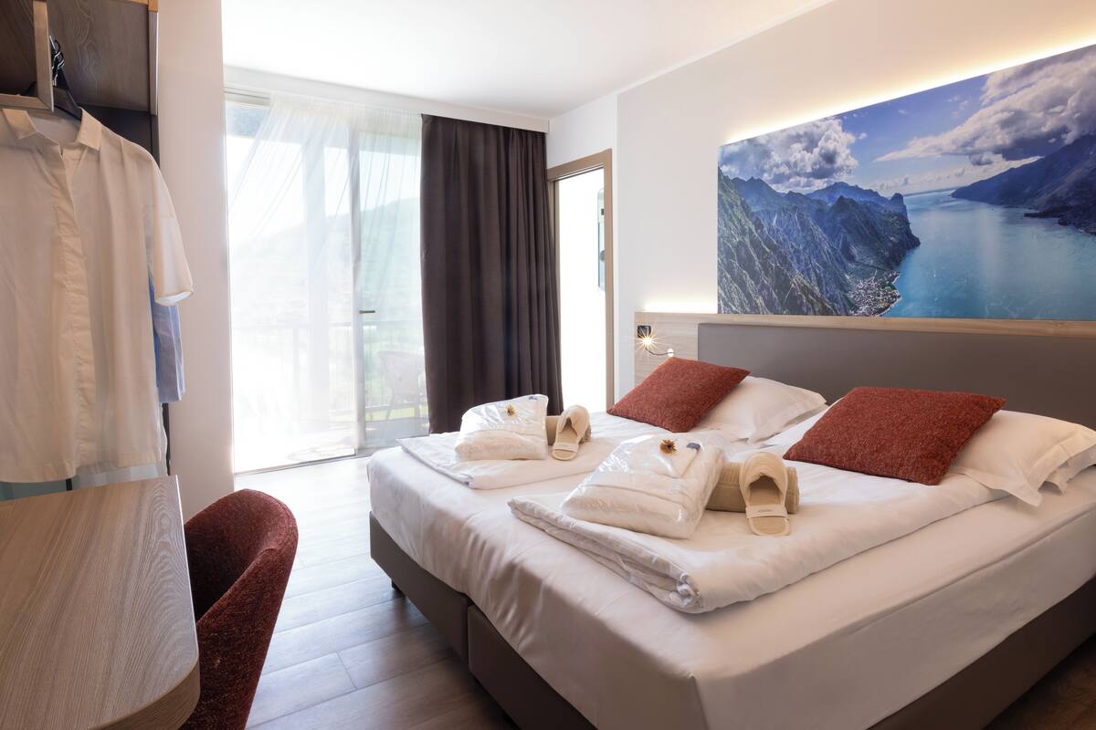 Une chambre d’hôtel avec un lit, une chaise, une table et une grande fenêtre avec des rideaux.