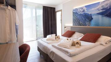 Ein Hotelzimmer mit Bett, einem Sessel, einem Tisch und einem großen Fenster mit Vorhängen.