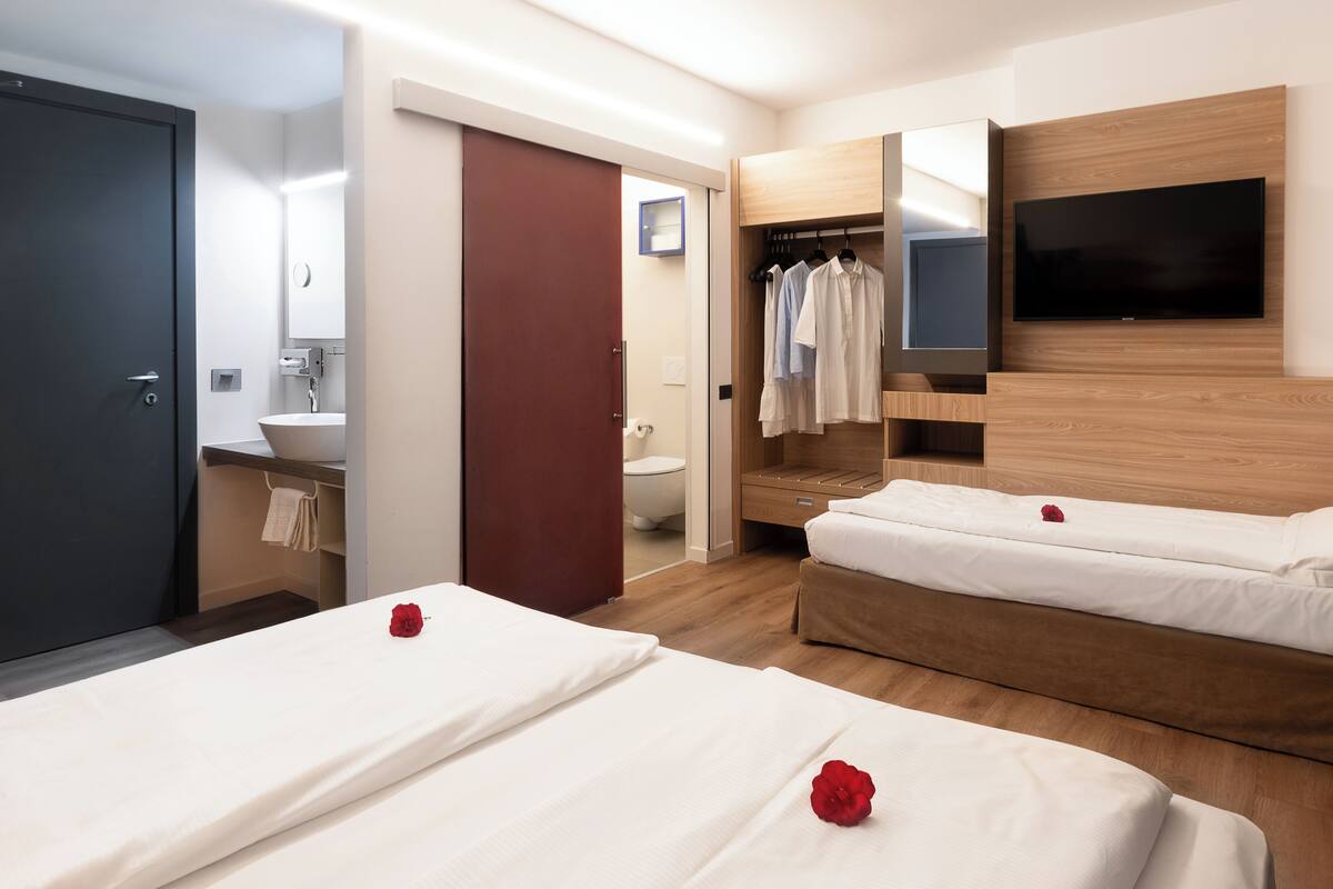 Une chambre d’hôtel avec deux lits, une télévision, une armoire en bois et une salle de bain équipée d’un lavabo et de toilettes.