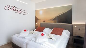 Une chambre d’hôtel moderne avec un grand lit, du linge de lit blanc, une fleur rouge posée sur l’oreiller et une œuvre d’art murale représentant un paysage paisible.