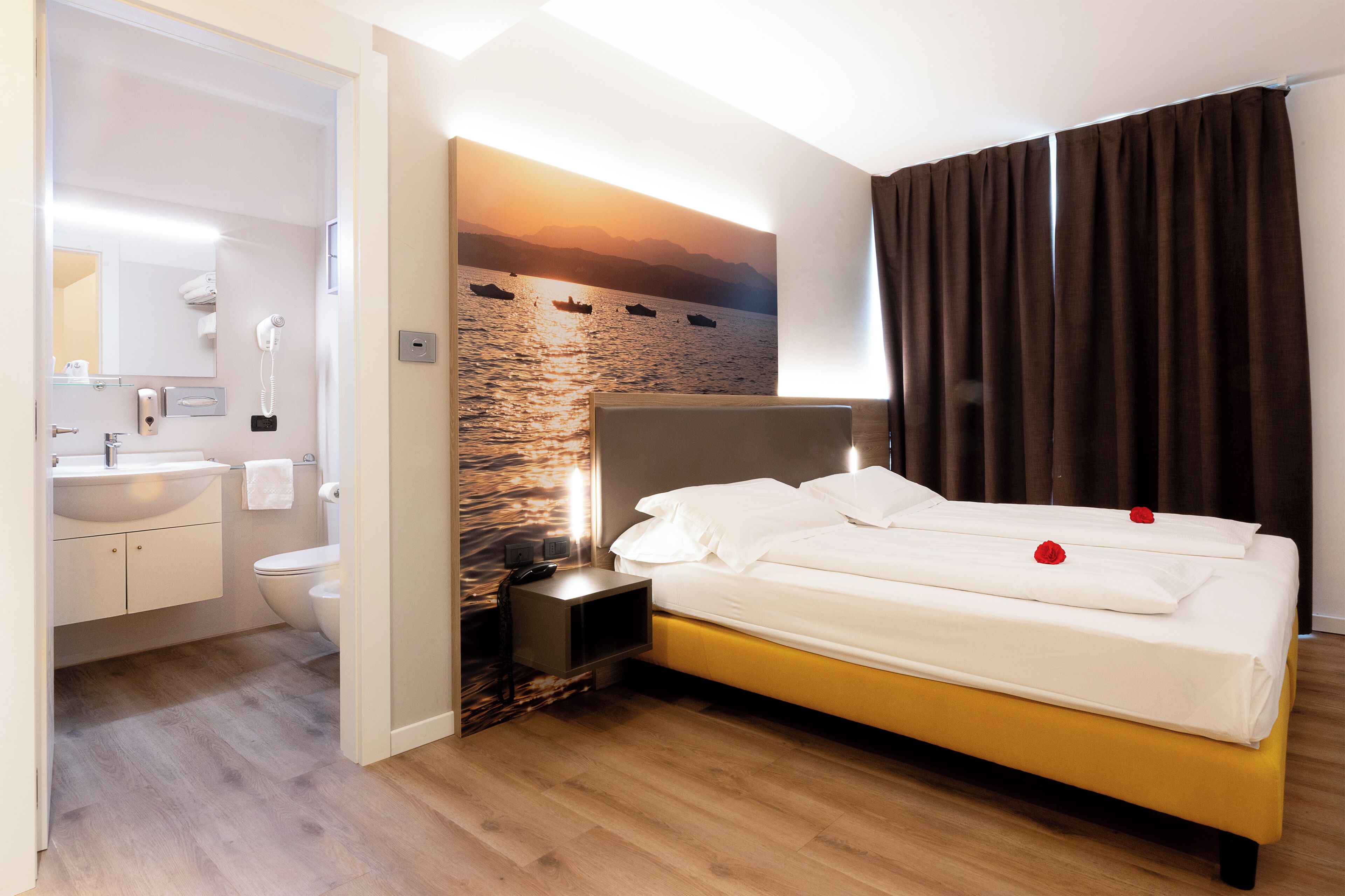 Une chambre d’hôtel comprenant un lit, une table de chevet, une salle de bain avec un lavabo et des toilettes, et un téléphone fixé au mur.