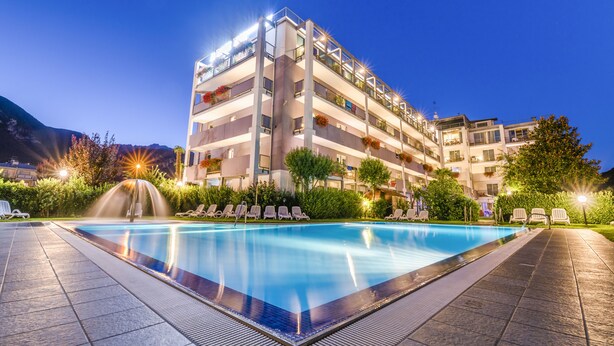 Een meerlaags hotel met een zwembad, terras en een fontein.