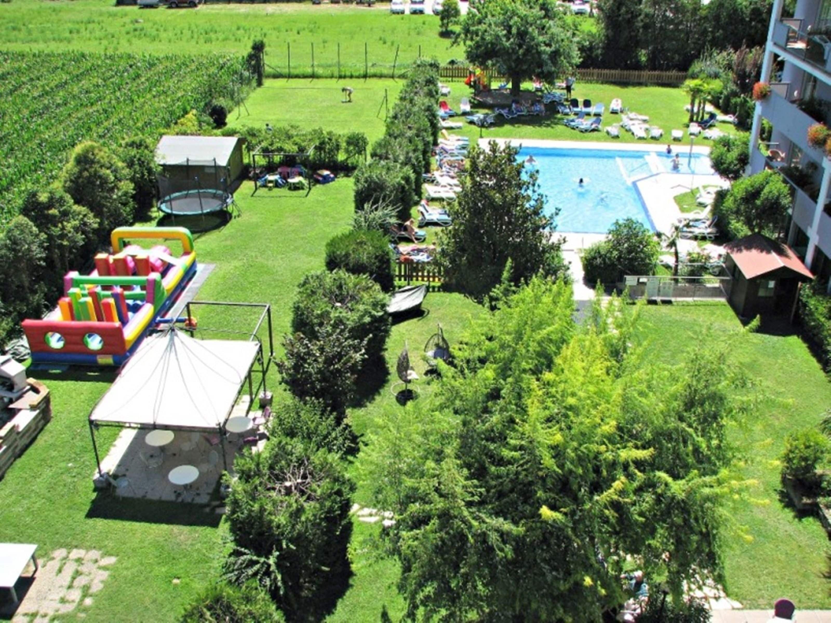 An aerial view of a hotel with a swimming pool, a children's play area, and a well-maintained lawn.