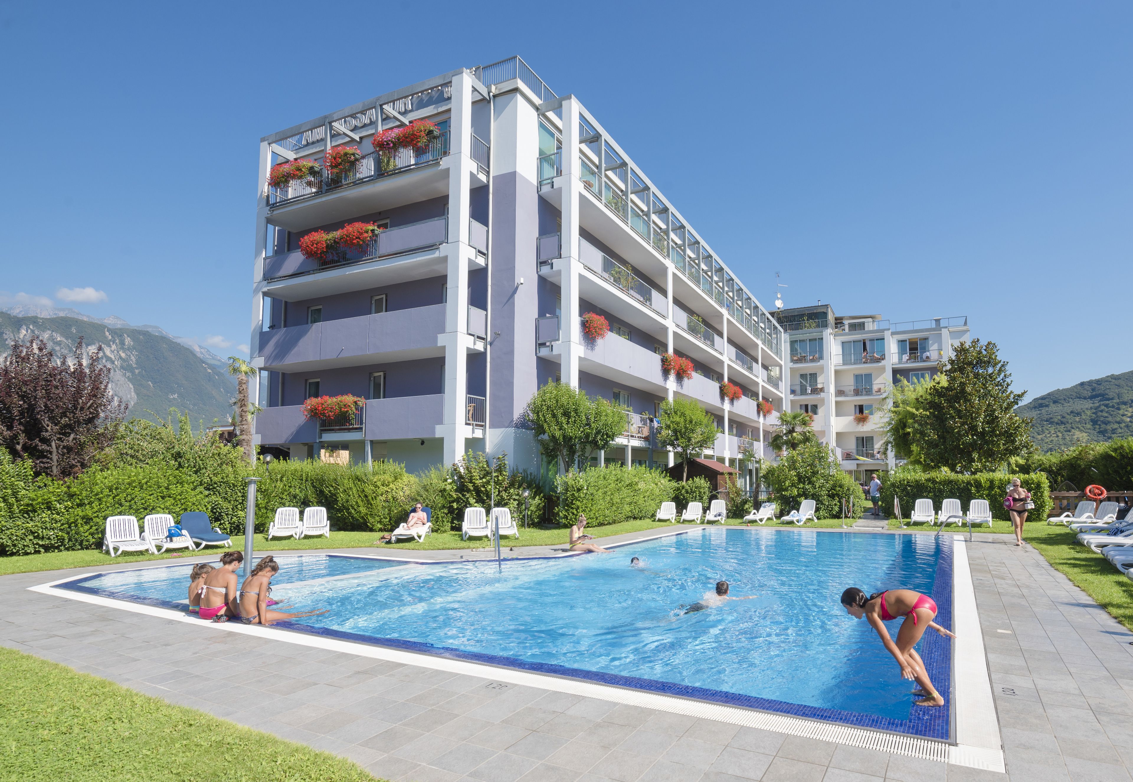 Un hotel con piscina, varios balcones con jardineras y vistas a las montañas.