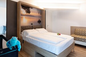 Una habitación de hotel con cama, mesita de noche, televisor montado en la pared y un peluche.