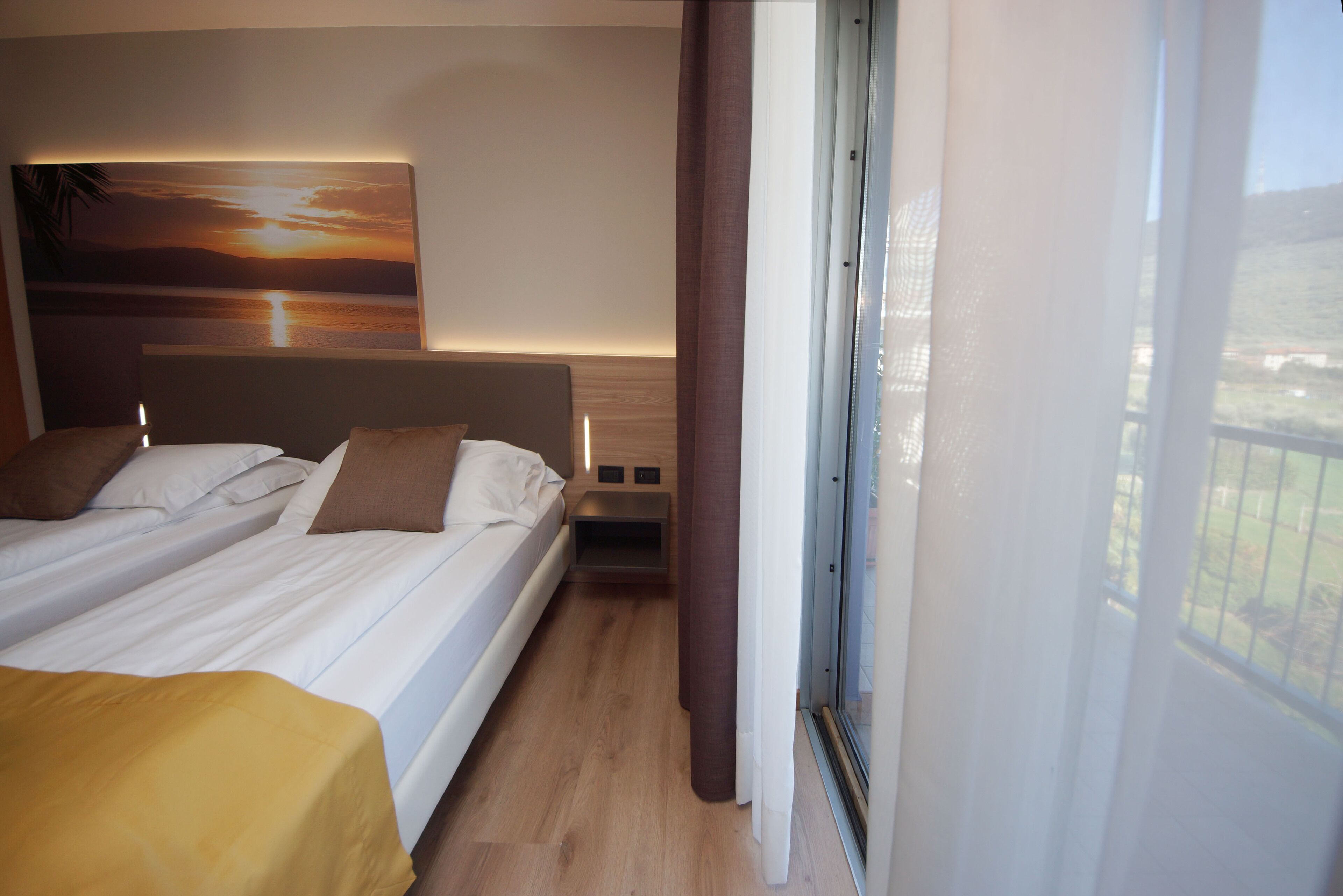 A hotel room with a bed, a bedside table, and a window with curtains.