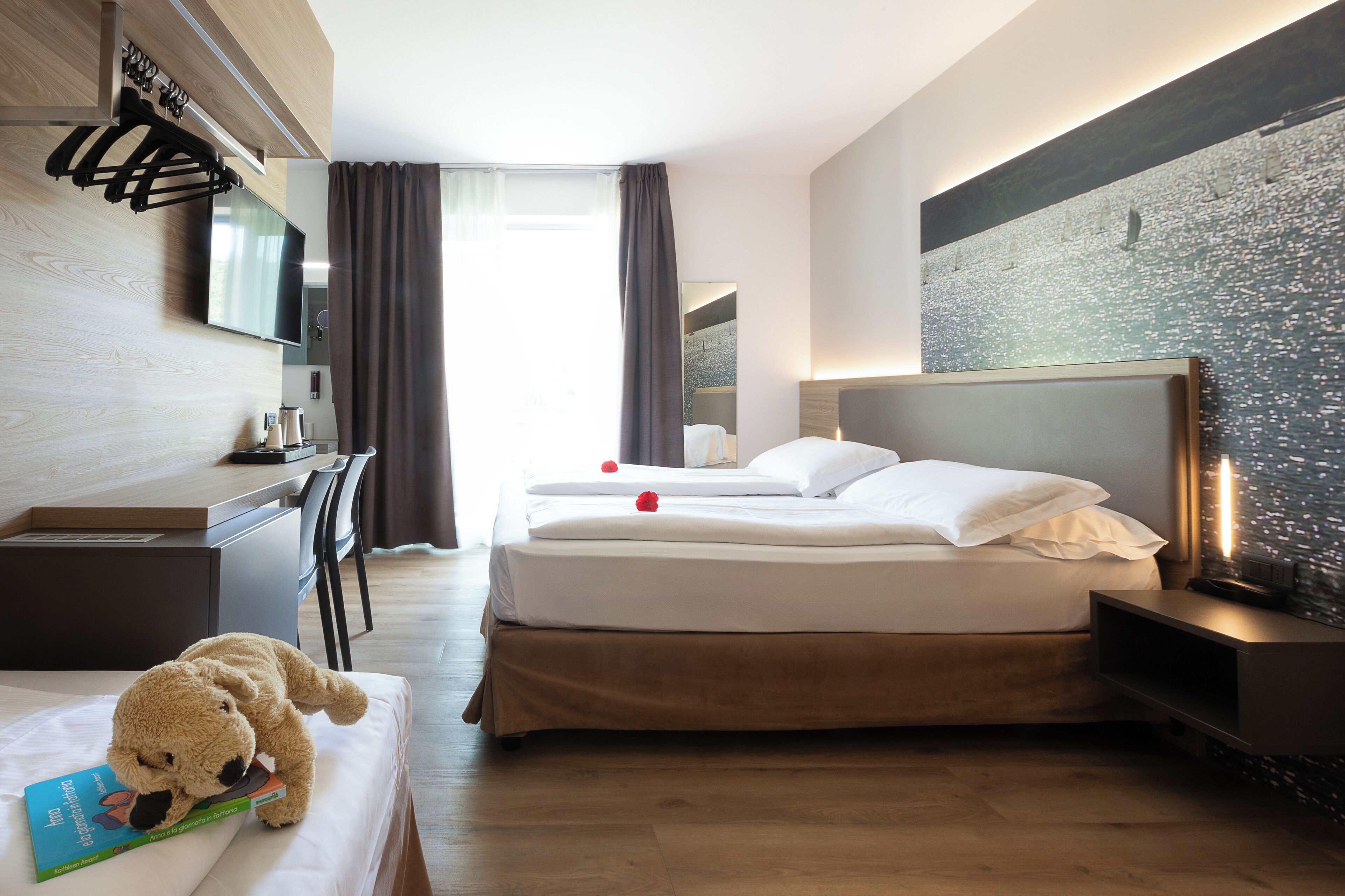 Une chambre d’hôtel avec un lit, une table de chevet, une télévision et un ours en peluche sur le lit.