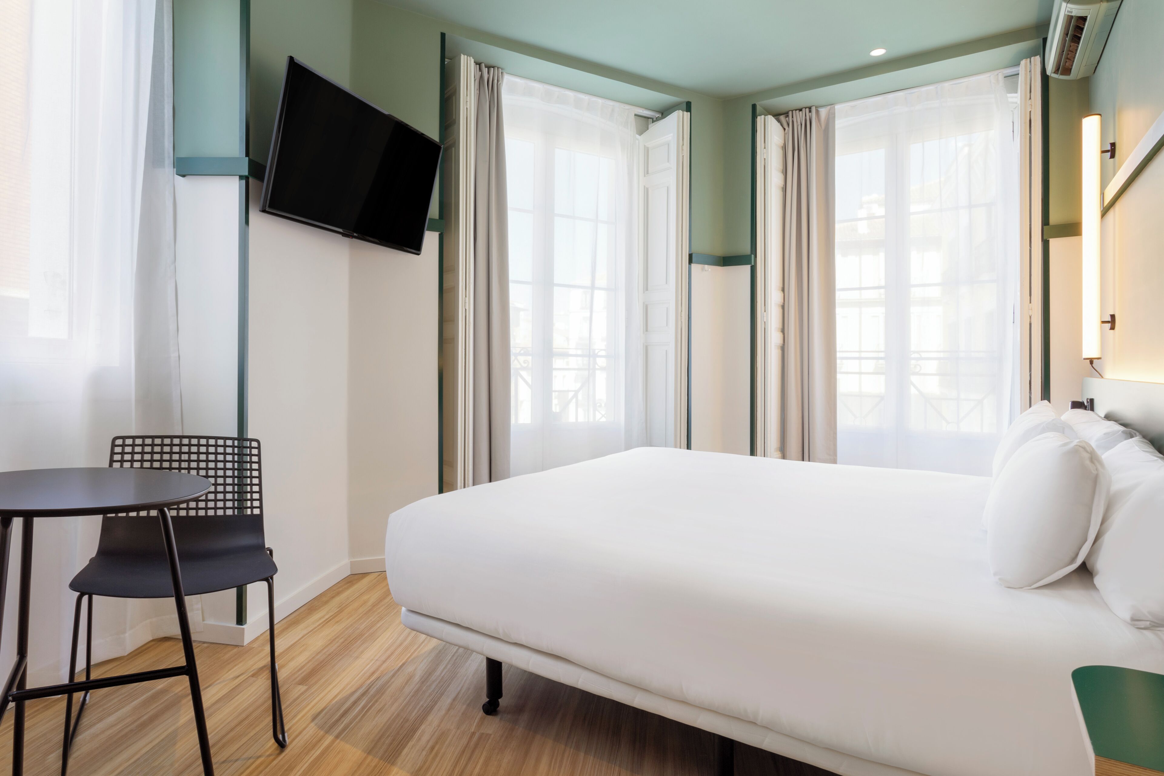 A hotel room with a bed, a TV mounted on the wall, a chair, and a table.