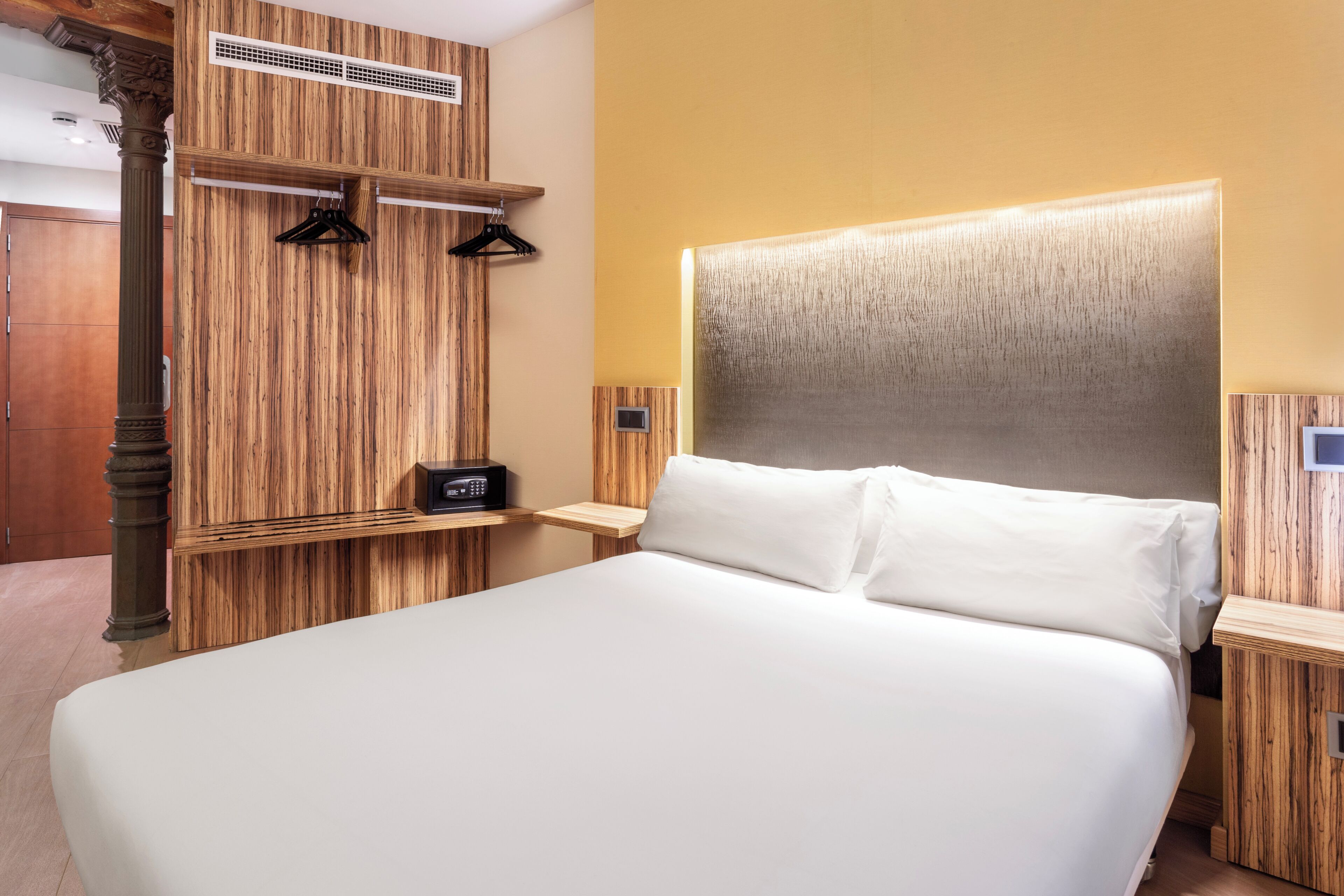 A hotel room with a large bed, wooden paneling on the walls, a small bedside table, and a wall-mounted radio.