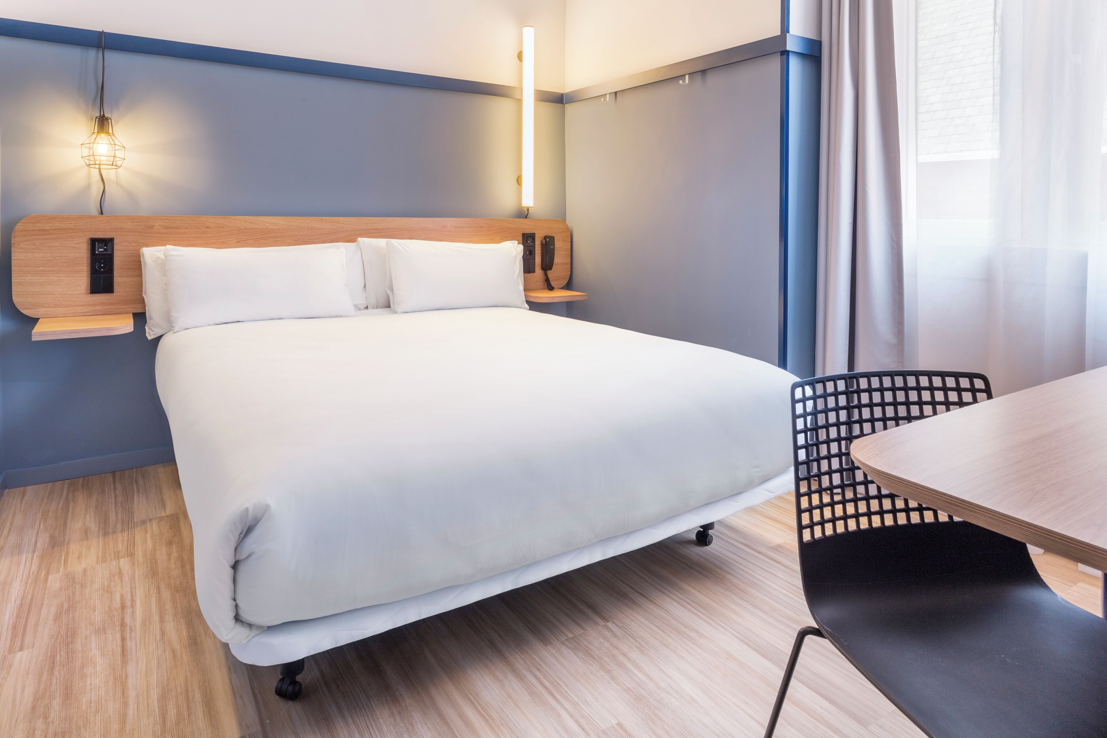 A neatly made bed with a wooden headboard, a bedside table with a lamp, and a chair.