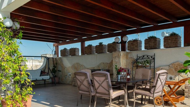 An outdoor patio with a table and chairs, potted plants, and a stone wall. - Aurora Rooms (Lecce)