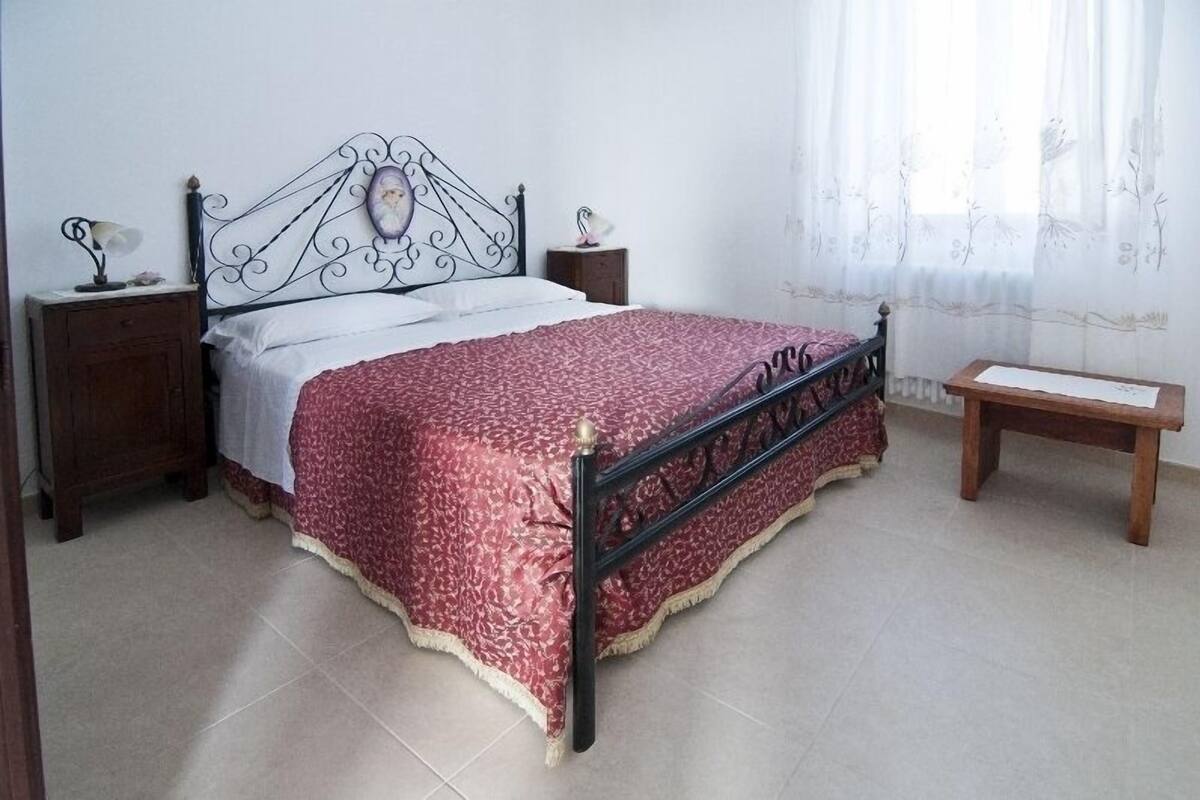 A bedroom with a bed, two nightstands, a wooden bench, and a window with curtains.