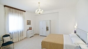 A bedroom with a bed, a chair, a wardrobe, and a chandelier. - Casa Vacanza La Scisa (Alessano)