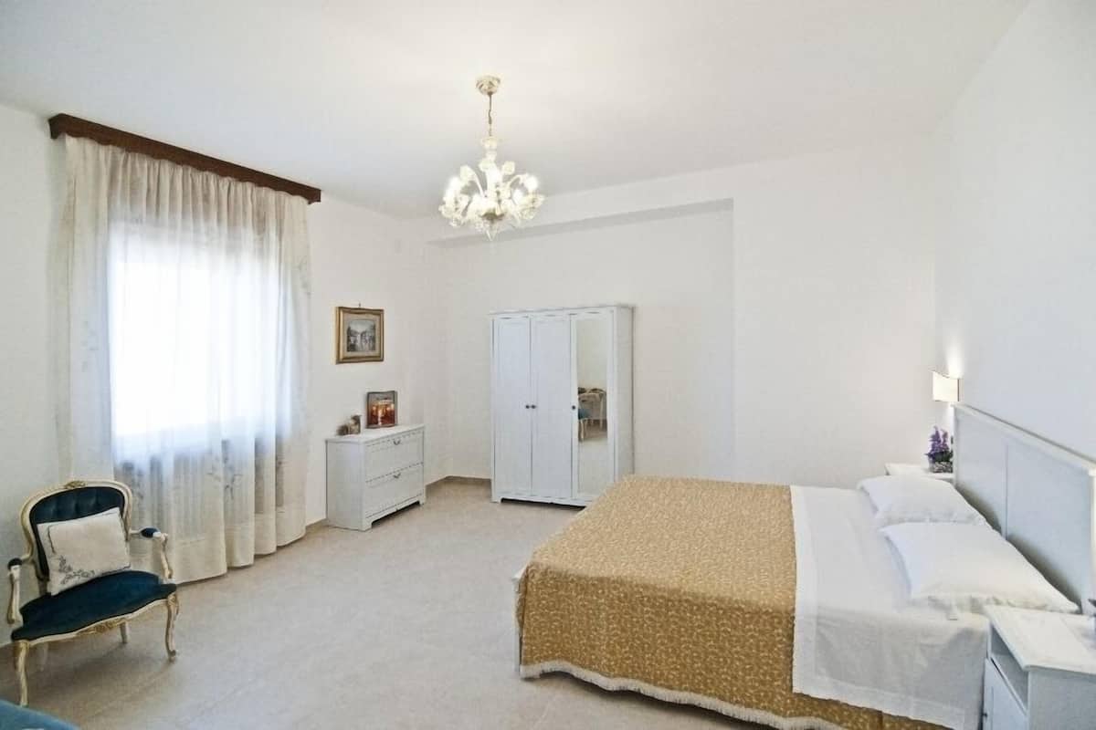 A bedroom with a bed, a chair, a wardrobe, and a chandelier.