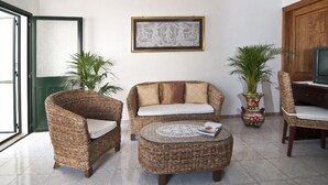 A living room with wicker furniture, a round coffee table, and two potted plants. - Casa Vacanza La Scisa (Alessano)