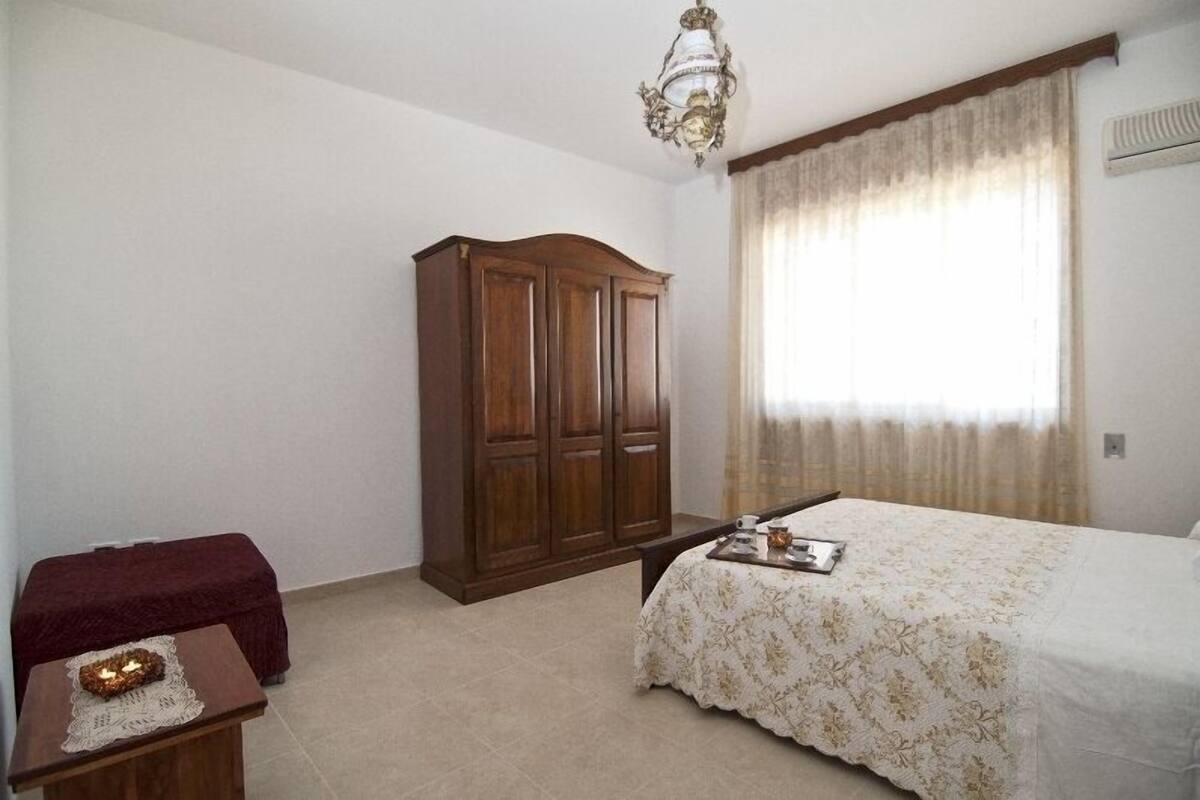 A bedroom with a bed, a wooden wardrobe, a bedside table with a candle, and a window with curtains.
