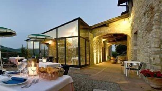 Un espace de restauration en plein air avec des tables dressées pour un repas, des murs en pierre et une structure vitrée.