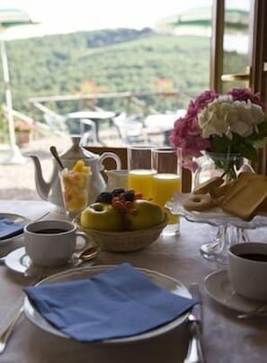 A breakfast table with a view of green hills, a pitcher, a bowl of fruit, and a vase of flowers. - Le Noci (Gaiole in Chianti)