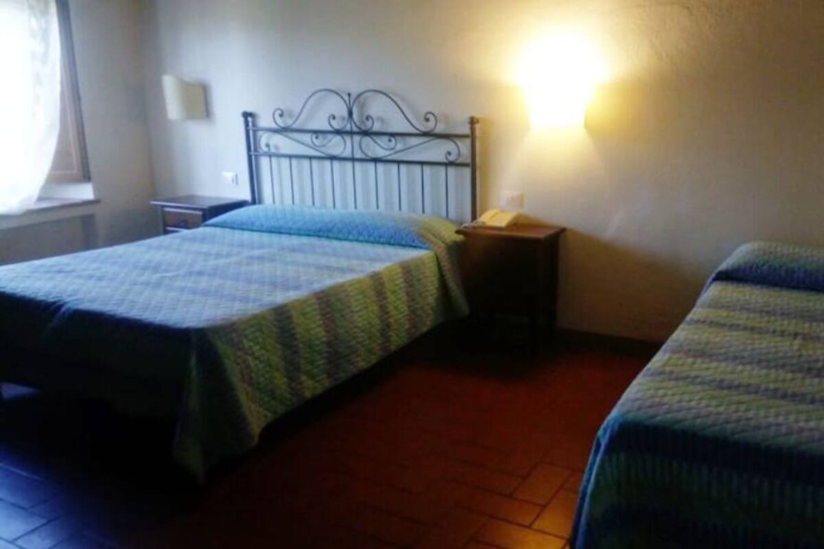 A room with two beds, a nightstand, a lamp, and a window.