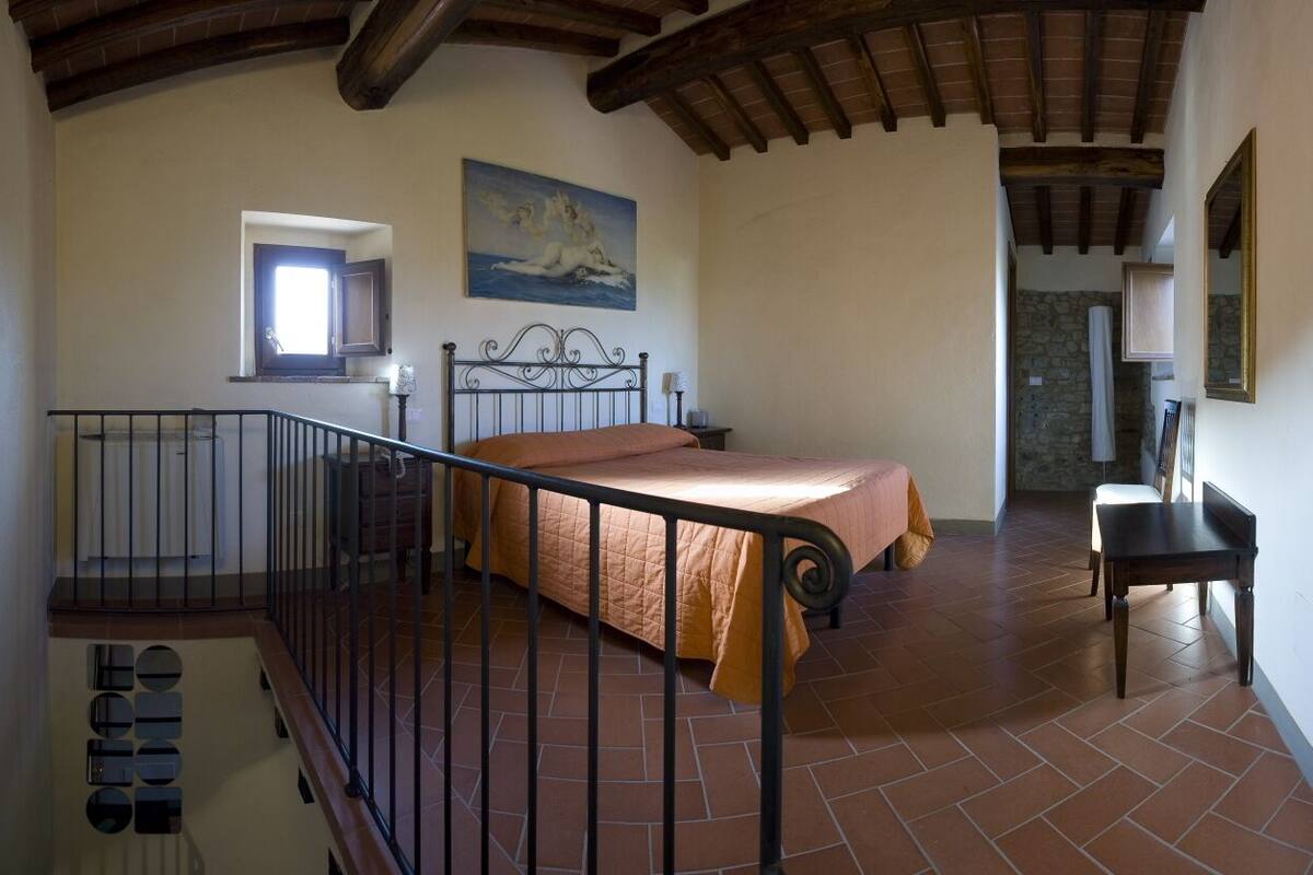 A bedroom with a bed, a window, a painting, and a staircase.